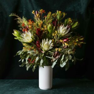 Australian Native flowers and foliage arranged in a tall white ceramic vase